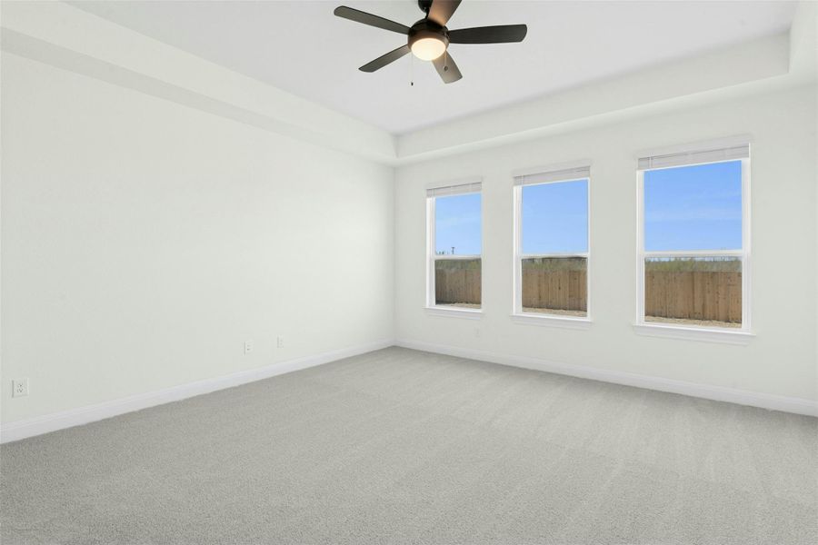 Spare room featuring light carpet, ceiling fan, and a tray ceiling
