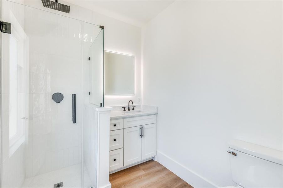 Bathroom with a shower with shower door, hardwood / wood-style flooring, vanity, and toilet