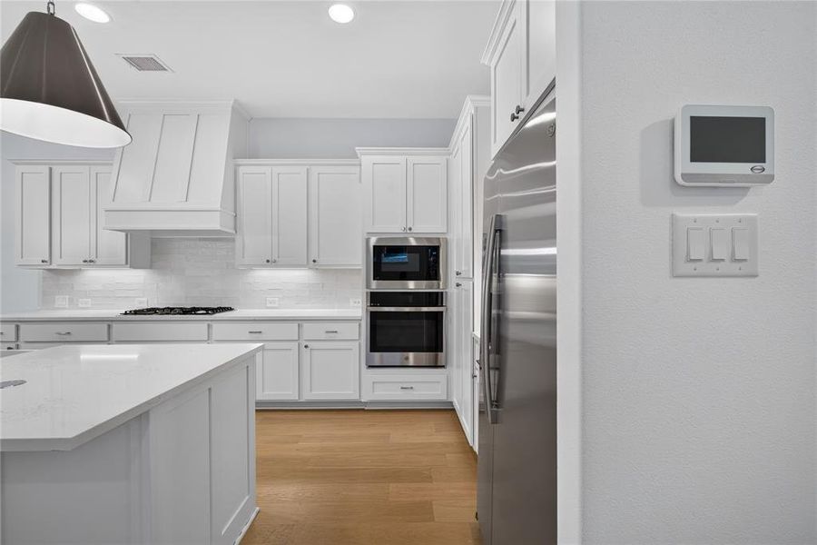 Contemporary kitchen featuring white cabinetry, a built-in oven, stainless steel refrigerator, and wood-finish flooring Contemporary kitchen featuring white cabinetry, a built-in oven, stainless steel refrigerator, and wood-finish flooring
