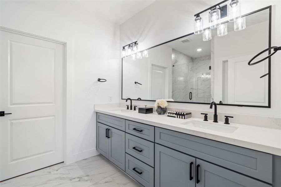 With soft gray cabinetry, quartz countertops, and chic black hardware, this bathroom combines sophistication with functionality.