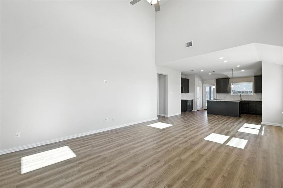 Unfurnished living room featuring light wood-style floors, a towering ceiling, a ceiling fan, and recessed lighting Unfurnished living room featuring light wood-style floors, a towering ceiling, a ceiling fan, and recessed lighting