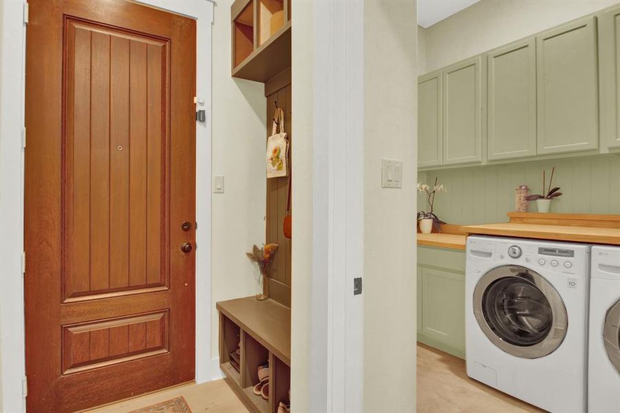 This is a compact laundry area with a front-loading washer, pastel green cabinetry, and a wooden countertop. There's a built-in nook for storage and a wooden panel garage door, suggesting efficient use of space.