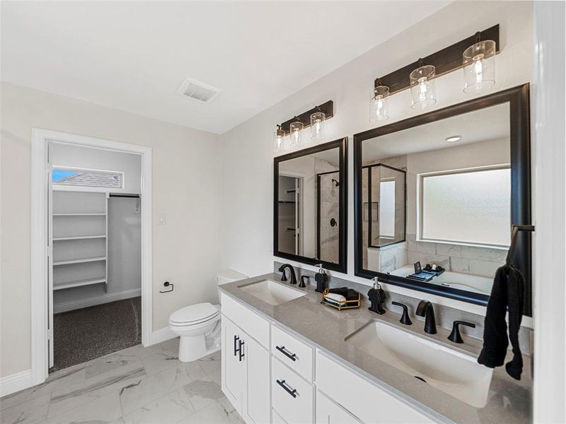 Full bath featuring marble finish flooring, toilet, baseboards, a walk in closet, and double vanity Full bath featuring marble finish flooring, toilet, baseboards, a walk in closet, and double vanity