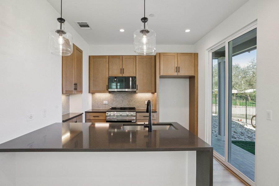 Kitchen with dark stone counters, a peninsula, decorative light fixtures, stainless steel appliances, and backsplash