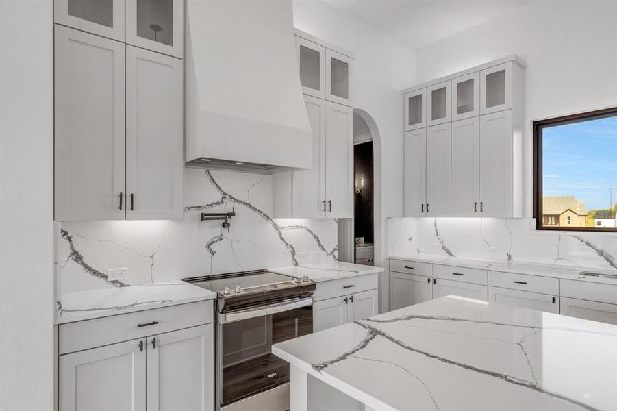 Kitchen with stainless steel range with electric cooktop, custom exhaust hood, and white cabinets