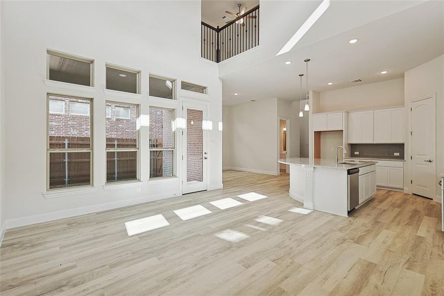 Kitchen featuring stainless steel dishwasher, a kitchen island with sink, decorative light fixtures, light hardwood / wood-style floors, and white cabinetry