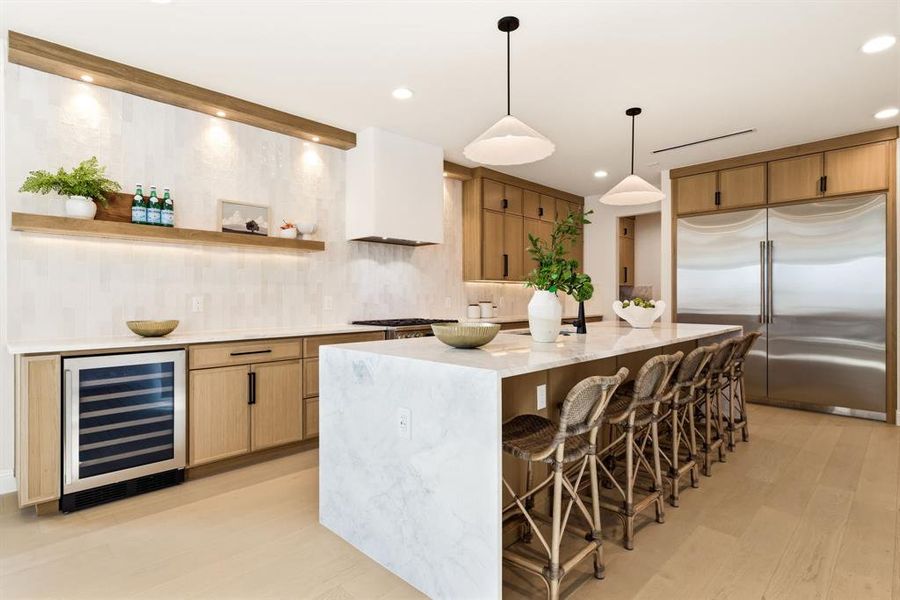 Kitchen with stainless steel built in fridge, light stone counters, a breakfast bar area, beverage cooler, and light wood-style floors