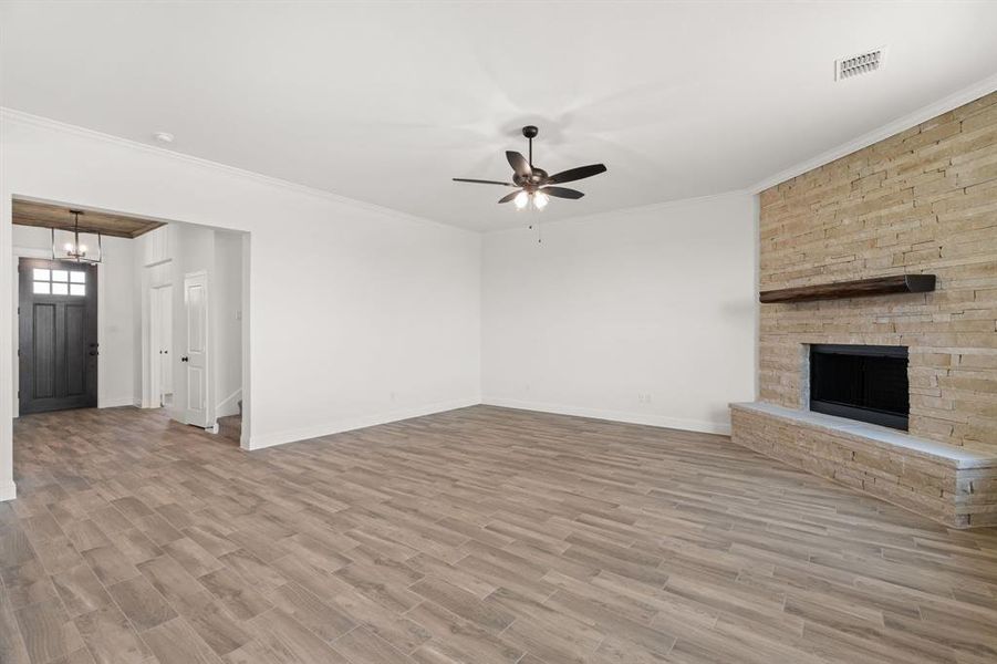 Unfurnished living room with a fireplace, light wood-type flooring, ornamental molding, and a ceiling fan Unfurnished living room with a fireplace, light wood-type flooring, ornamental molding, and a ceiling fan