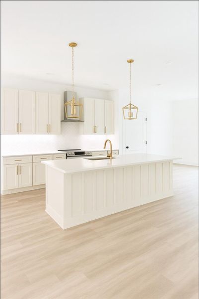 Kitchen featuring a spacious island, decorative light fixtures, wall chimney range hood, and light wood-type flooring