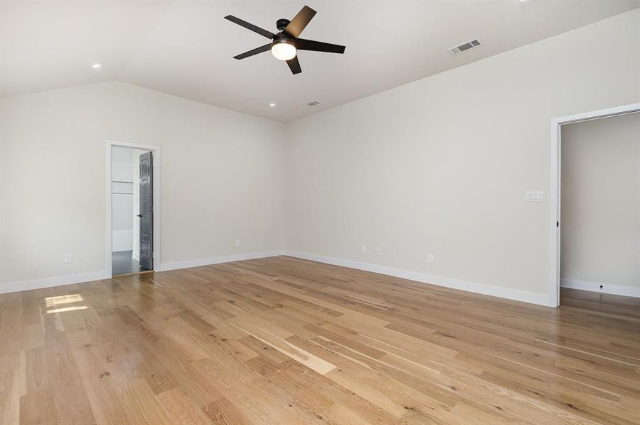 Unfurnished room with visible vents, baseboards, lofted ceiling, light wood-style flooring, and a ceiling fan