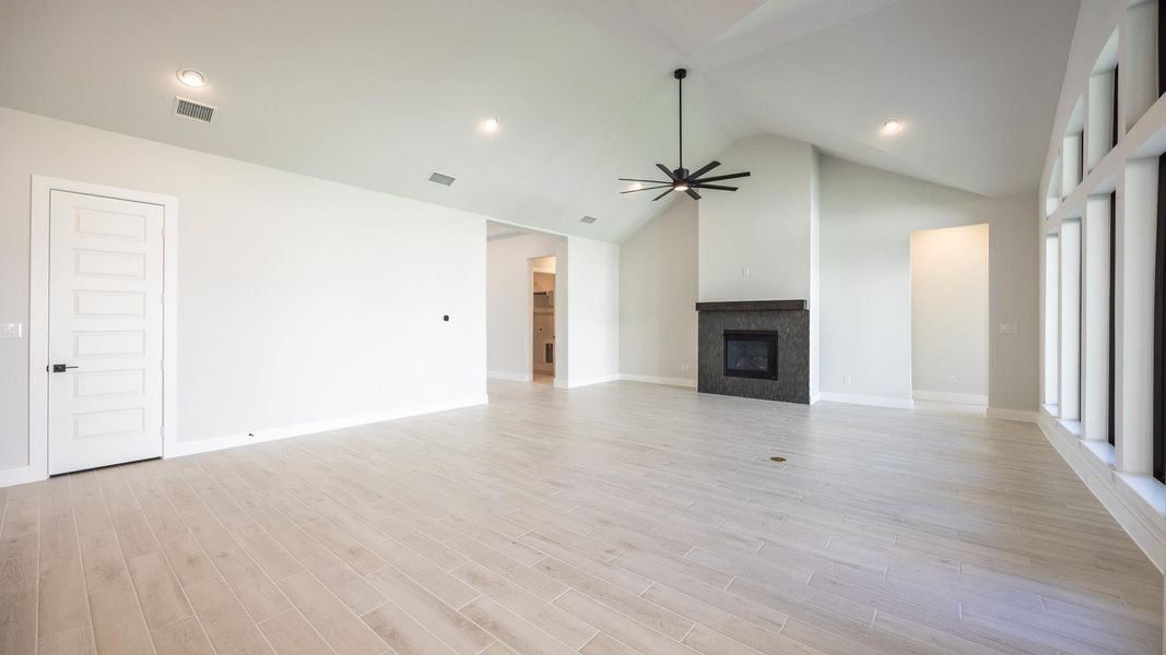 Unfurnished living room featuring a glass covered fireplace, recessed lighting, high vaulted ceiling, light wood finished floors, and ceiling fan