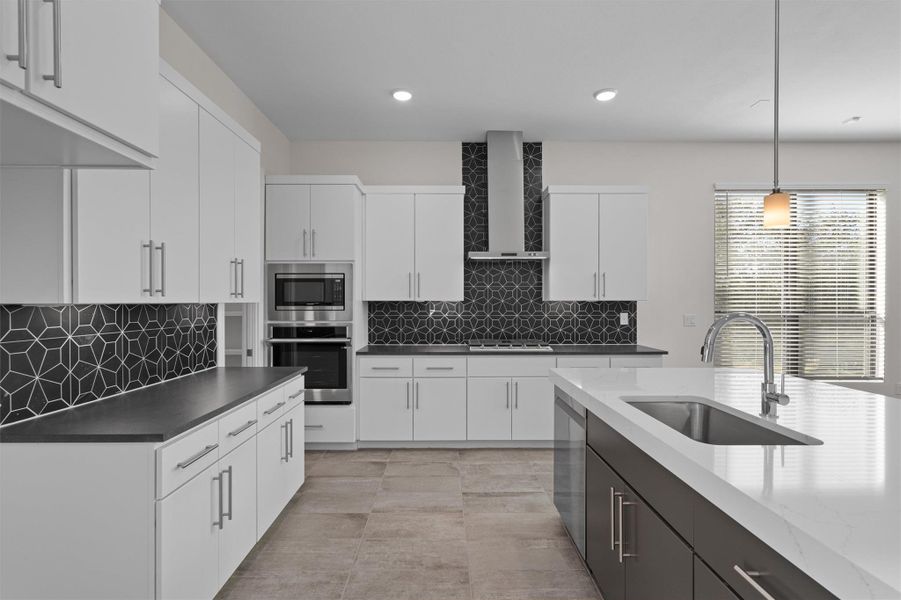 Kitchen with pendant lighting, white cabinetry, stainless steel appliances, wall chimney exhaust hood, and backsplash Kitchen with pendant lighting, white cabinetry, stainless steel appliances, wall chimney exhaust hood, and backsplash