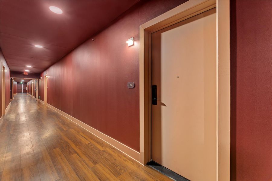 Rich wood plank flooring runs throughout a long, warmly lit common area corridor.