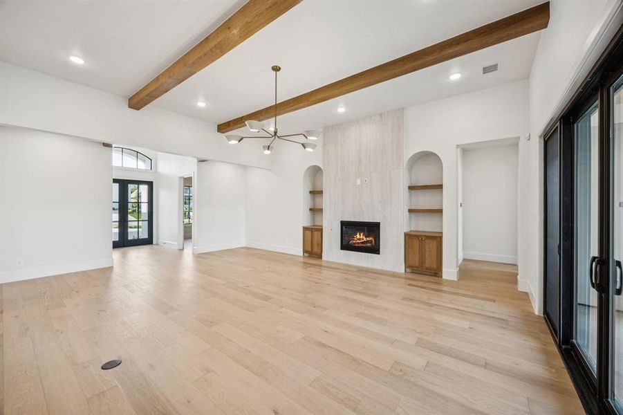 Unfurnished living room with a large fireplace, light wood finished floors, beamed ceiling, recessed lighting, and built in shelves Unfurnished living room with a large fireplace, light wood finished floors, beamed ceiling, recessed lighting, and built in shelves