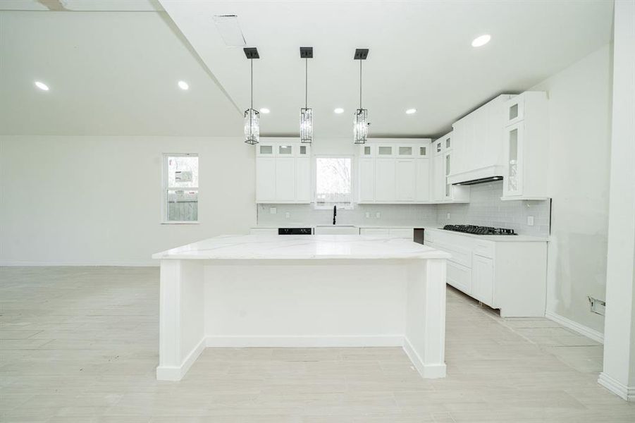 Kitchen featuring hanging light fixtures, a kitchen island, glass insert cabinets, white cabinets, and recessed lighting