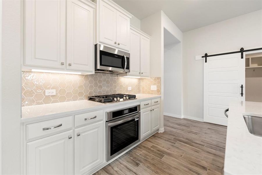 Kitchen with a barn door, white cabinetry, appliances with stainless steel finishes, light stone countertops, and decorative backsplash