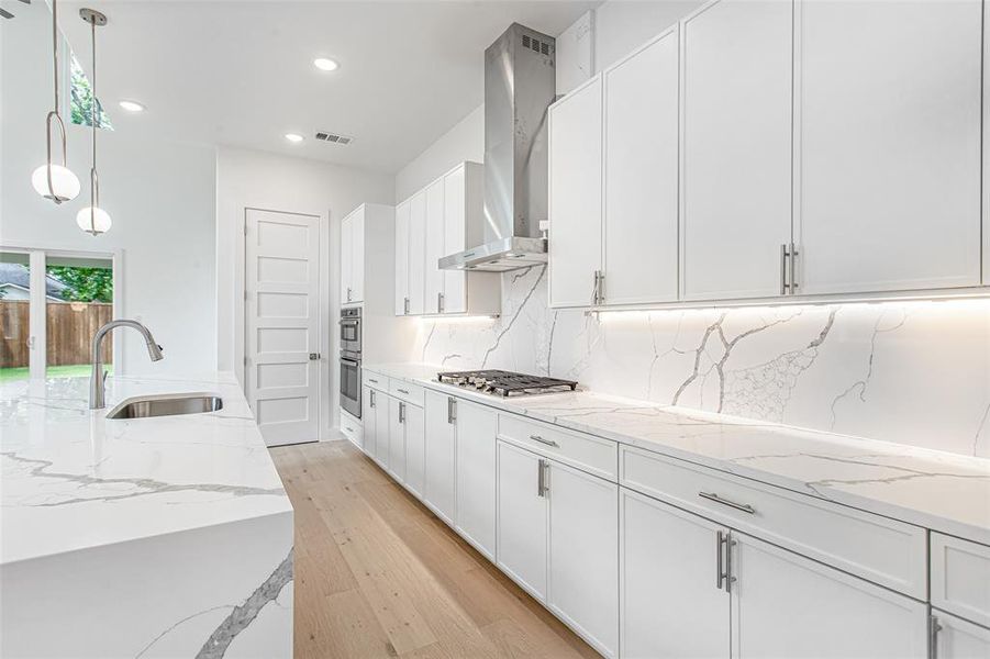 Kitchen featuring wall chimney range hood, a sink, appliances with stainless steel finishes, white cabinetry, and decorative backsplash