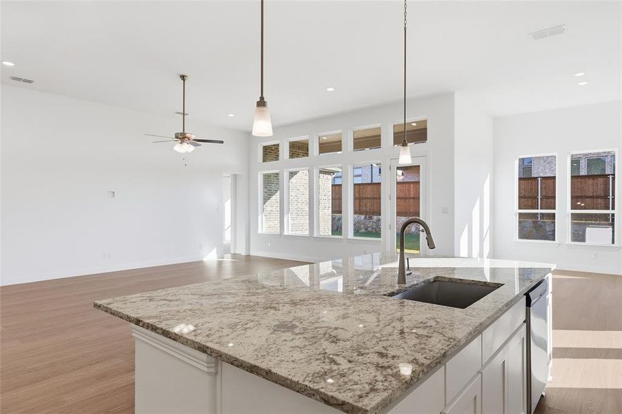 Kitchen featuring light stone countertops, a center island with sink, open floor plan, pendant lighting, and white cabinets Kitchen featuring light stone countertops, a center island with sink, open floor plan, pendant lighting, and white cabinets
