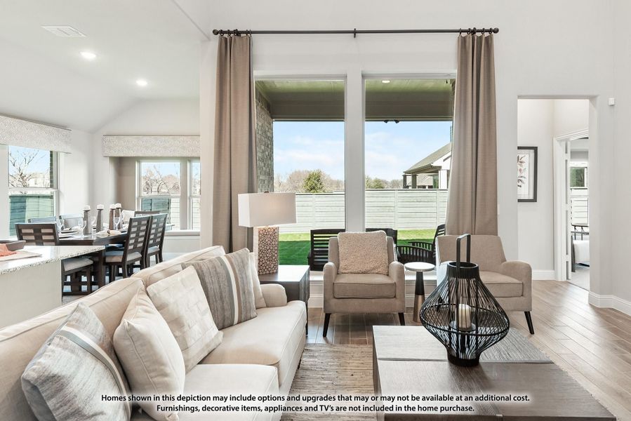 Open-concept living room with neutral sofa, hardwood floors, and large windows overlooking a backyard patio