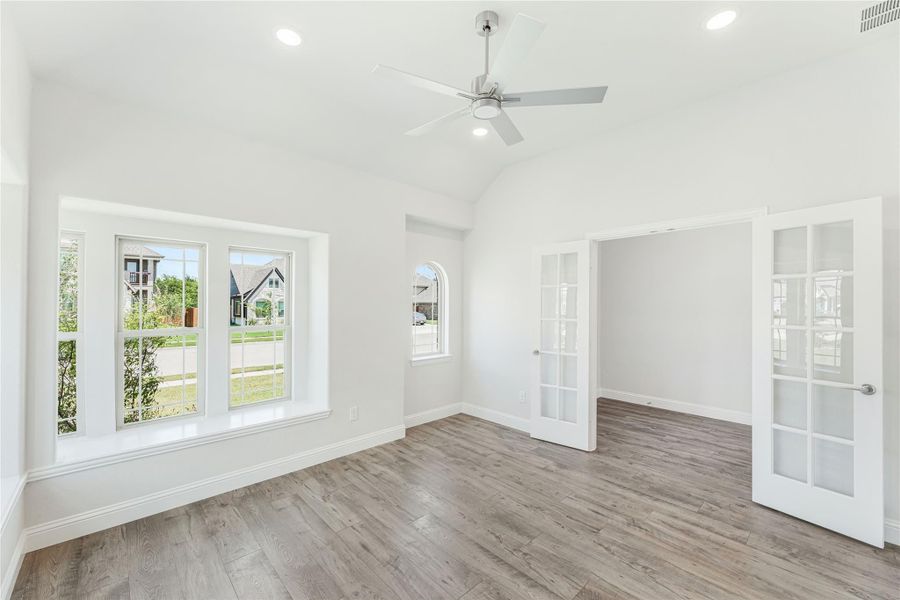 Bright empty room with vaulted ceiling, hardwood floors, ceiling fan, and French doors Bright empty room with vaulted ceiling, hardwood floors, ceiling fan, and French doors