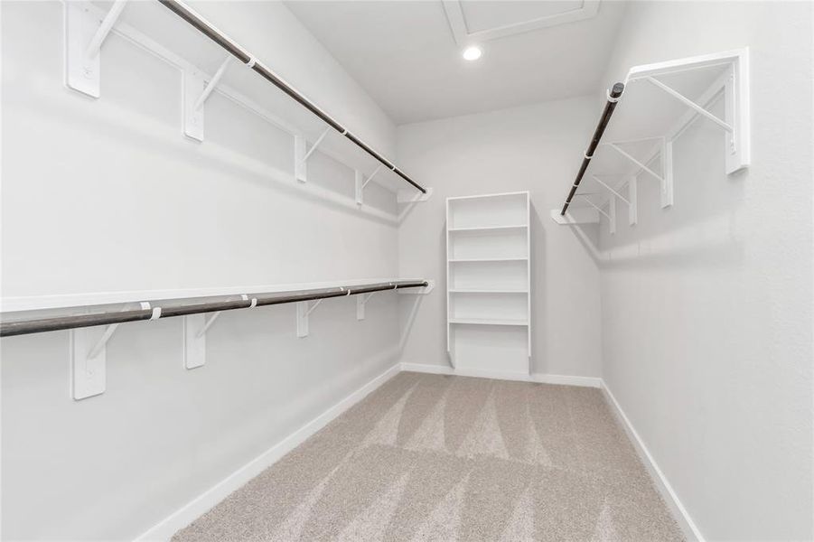 Discover luxury in this expansive walk-in closet, adorned with high ceilings and luxurious carpet. Immerse yourself in the inviting atmosphere created by warm paint tones, utilize the convenience of built-in shelving, and experience the modern and functional retreat accentuated by dark finishes. Sample photo of completed home with similar floor plan. As-built interior colors and selections may vary