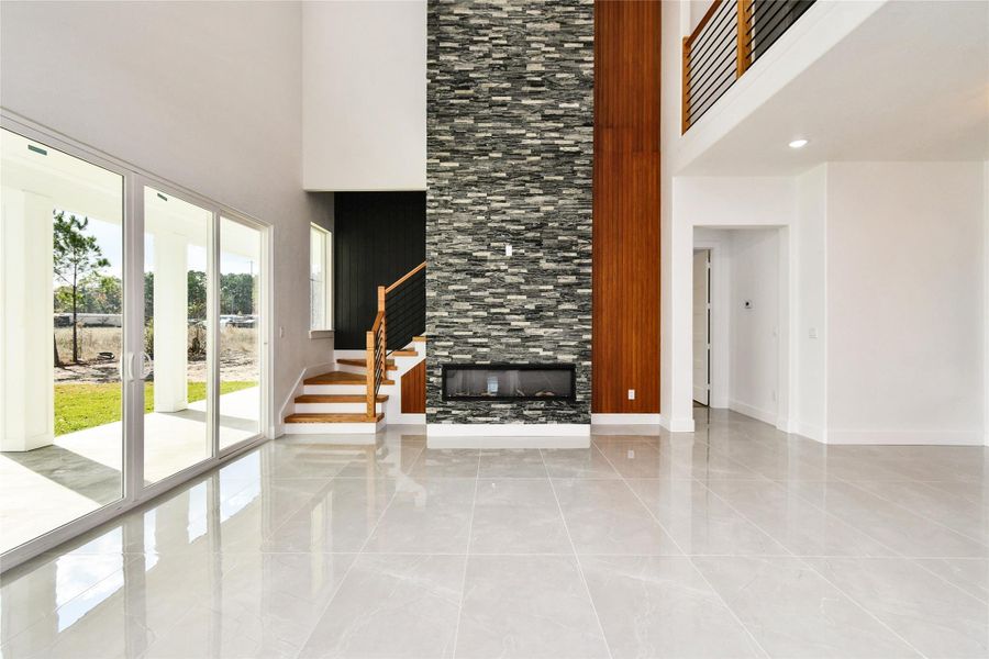 The heart of the home features a dramatic floor-to-ceiling stone fireplace. The sleek linear design is flanked by warm wood paneling and a modern staircase with custom iron railings.