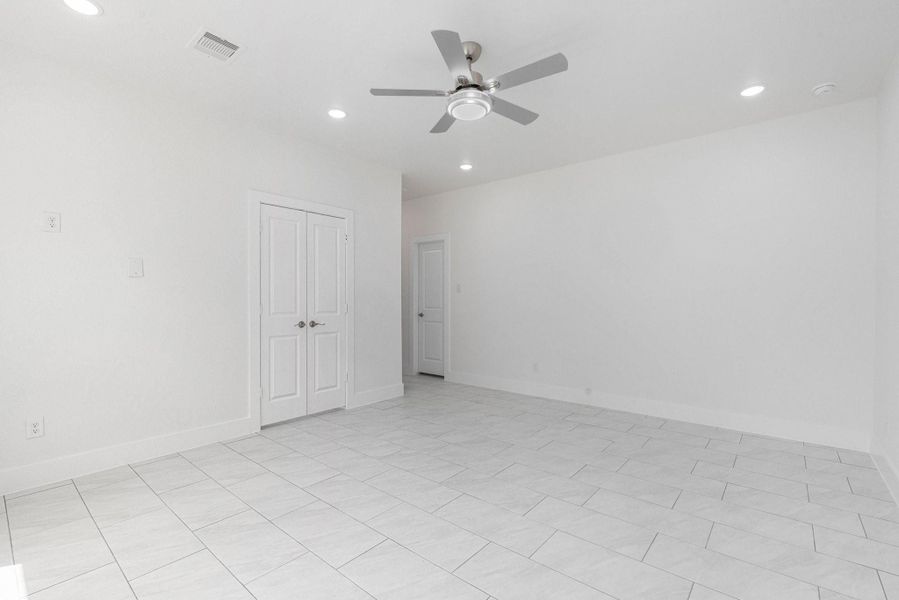 This spacious room features clean white walls and tile flooring, complemented by a ceiling fan and recessed lighting. A double-door closet and additional doorway provide ample storage and access. This spacious room features clean white walls and tile flooring, complemented by a ceiling fan and recessed lighting. A double-door closet and additional doorway provide ample storage and access.