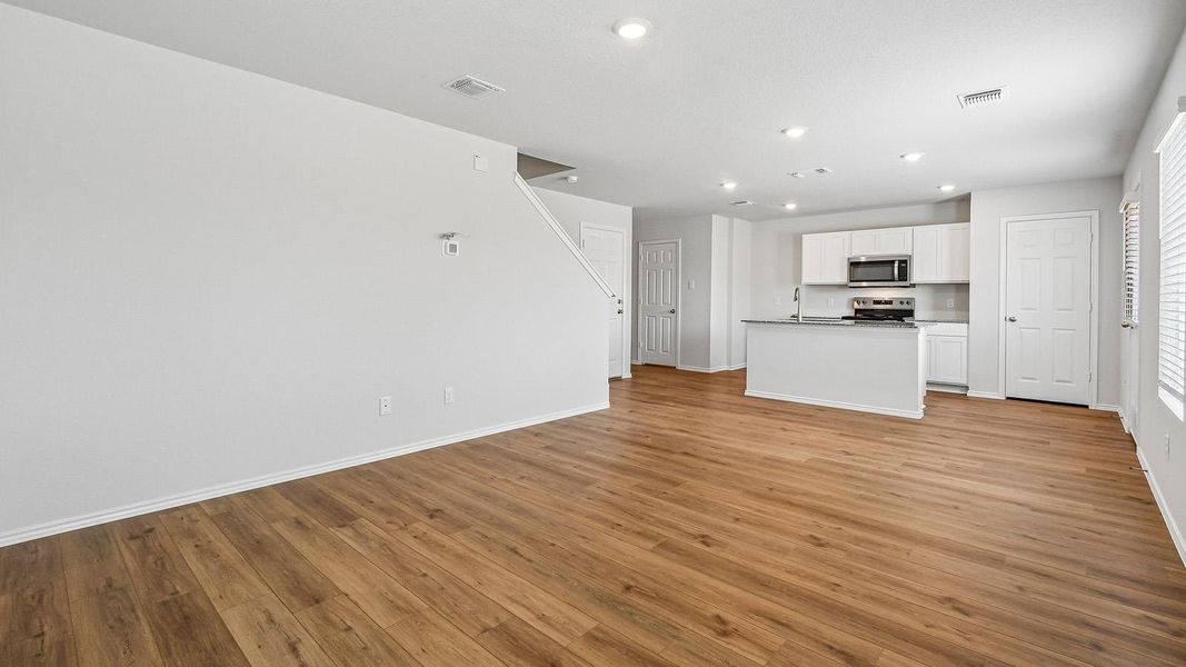 A well-lit, open-concept living area seamlessly transitions into a contemporary kitchen, boasting rich wood flooring.
