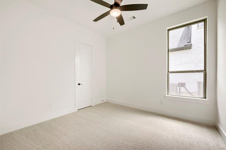 Carpeted room featuring a ceiling fan with integrated lighting, a paneled door with dark hardware, and a framed window Carpeted room featuring a ceiling fan with integrated lighting, a paneled door with dark hardware, and a framed window