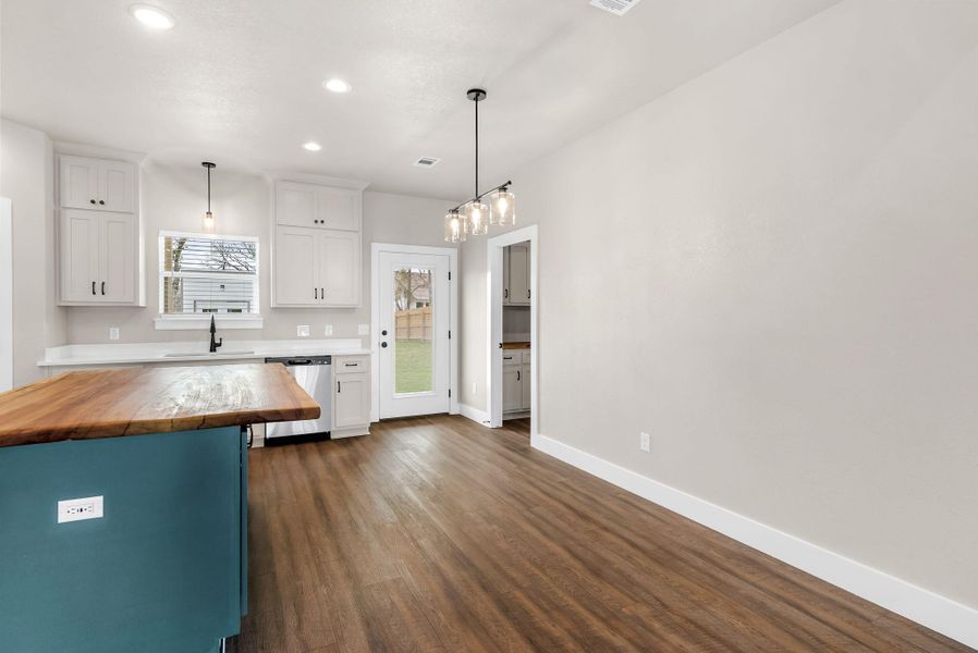 Kitchen with butcher block countertops, decorative light fixtures, dishwasher, two tone cabinets, and dark wood-style flooring