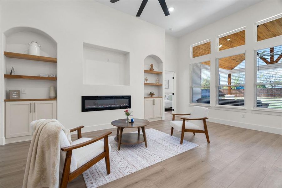 Living area with built in shelves, ceiling fan, a glass covered fireplace, light wood-type flooring, and recessed lighting Living area with built in shelves, ceiling fan, a glass covered fireplace, light wood-type flooring, and recessed lighting