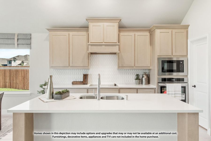 Kitchen with light wood cabinets, white island with double sink, and stainless steel built-in appliances