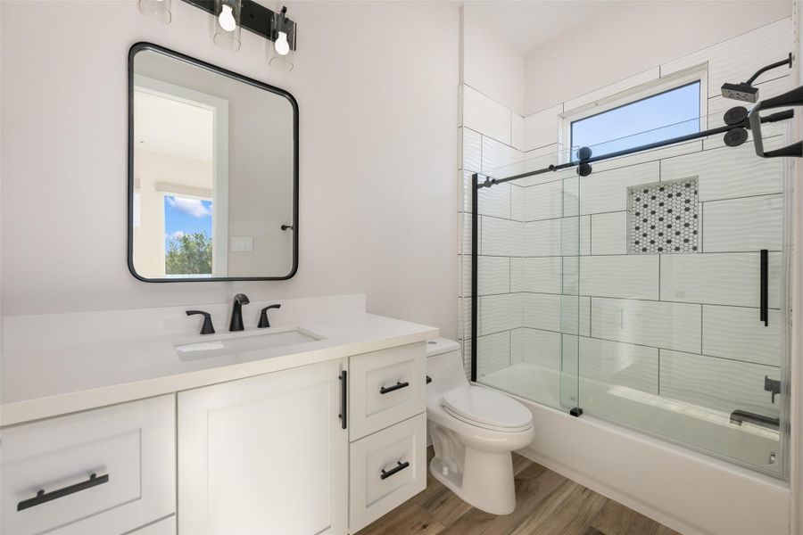 Full bathroom with wood-type flooring, enclosed tub / shower combo, vanity, and toilet