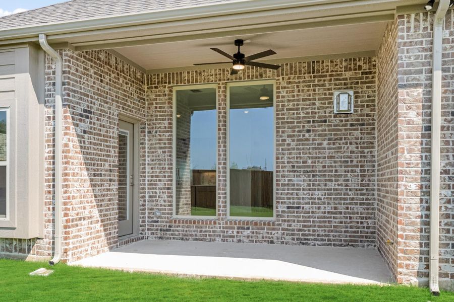 Covered back patio with ceiling fan, brick exterior, large window, and concrete floor