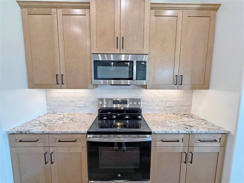 Kitchen featuring stainless steel appliances, light stone countertops, decorative backsplash, and light brown cabinetry