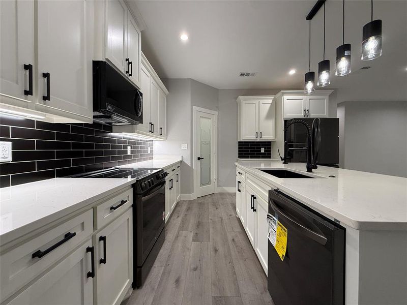 Kitchen with decorative light fixtures, black appliances, light stone counters, white cabinets, and light wood-style floors