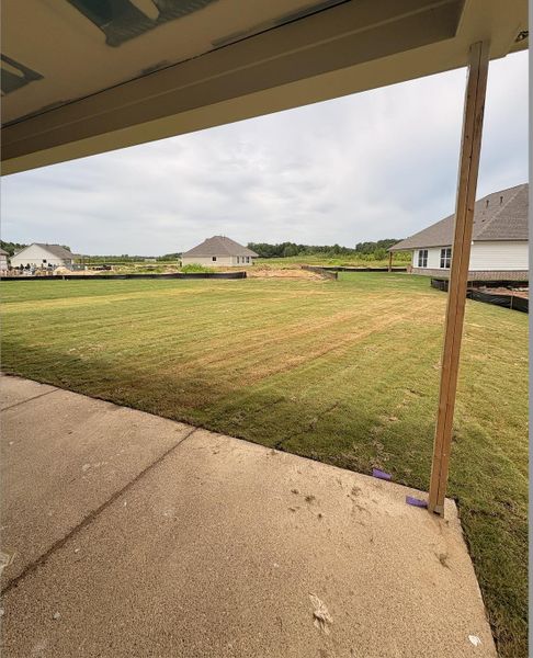 Spacious concrete patio overlooking an expansive lawn with a backdrop of green space and distant residential structures Spacious concrete patio overlooking an expansive lawn with a backdrop of green space and distant residential structures