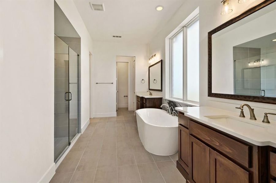 Bathroom with two vanities, a freestanding tub, a stall shower, light tile patterned flooring, and recessed lighting