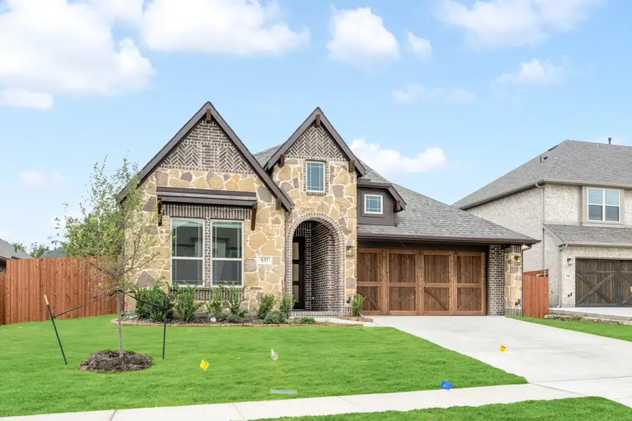 Two-story home with stone and brick exterior, arched entry, two-car garage, and green front lawn