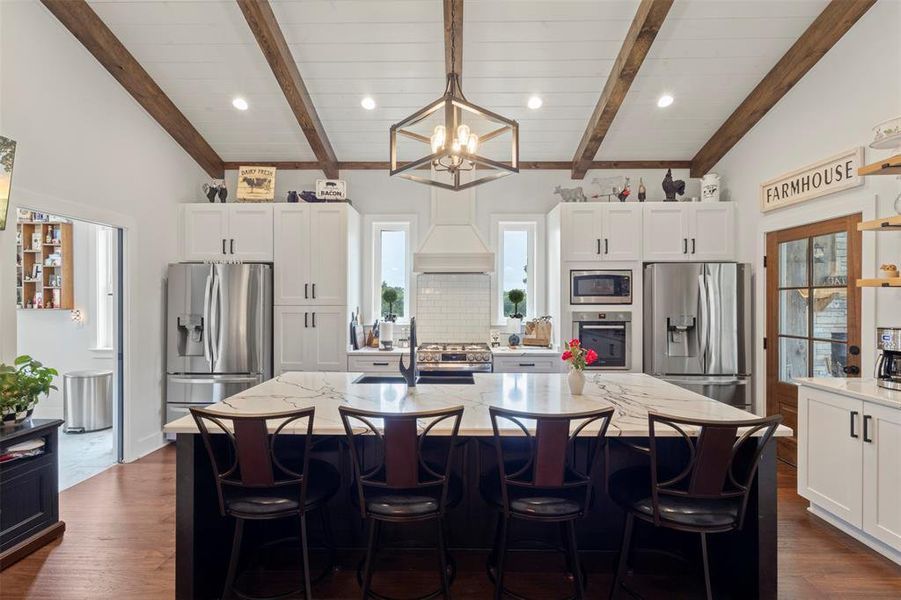 Expansive farmhouse-style kitchen featuring soaring beamed ceilings, a statement island with quartz countertops, and a gas range with convection oven—designed for both everyday cooking and effortless entertaining.