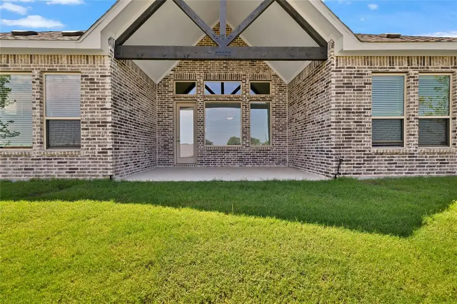 Doorway to property featuring brick siding, a patio, and a lawn