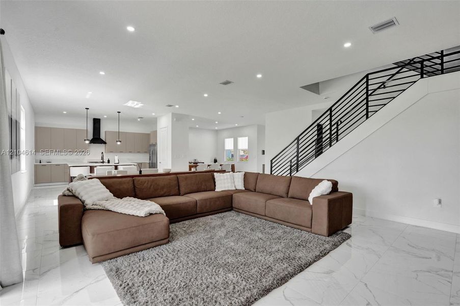 Open-concept living space featuring high ceilings, recessed lighting, large format tile flooring, and a contemporary staircase with black metal railings