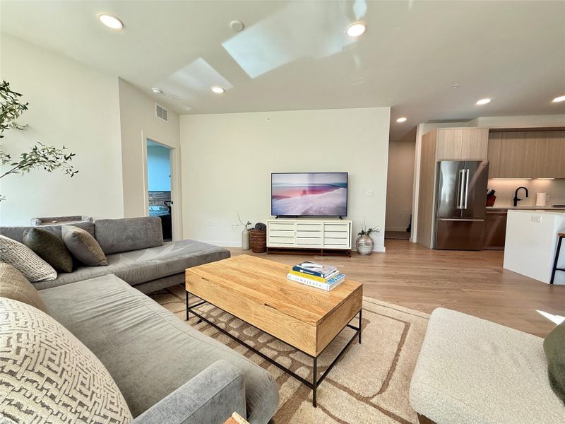 Natural wood flooring extends throughout this generous living space, leading to a modern kitchen.