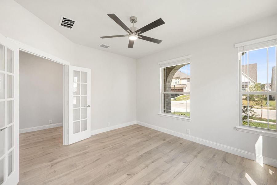 Empty room with light wood floors, ceiling fan, two windows, and French doors