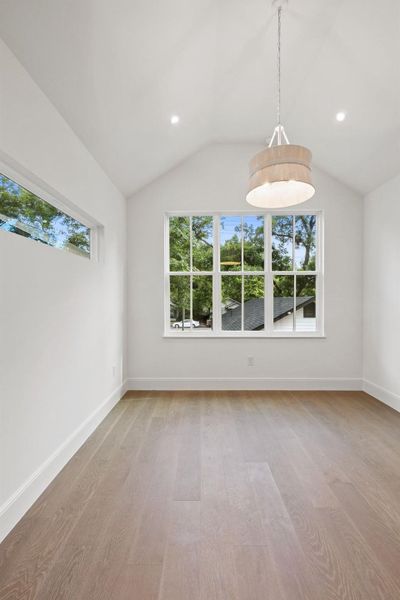 Natural light streams into this room through a large window, illuminating the hardwood flooring and vaulted ceiling.