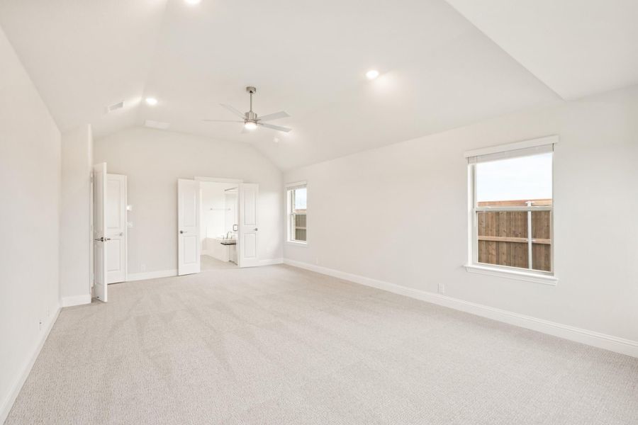 Spacious bedroom with vaulted ceiling, ceiling fan, carpet flooring, and two windows leading to ensuite bathroom.