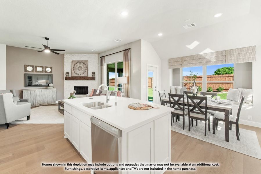 Open-concept kitchen with white island and sink, flowing into dining area and living room with brick fireplace