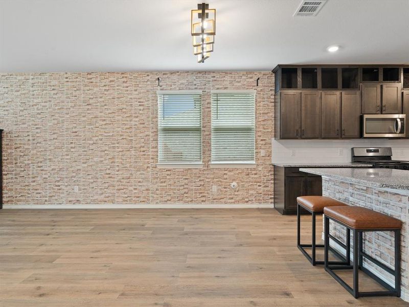 Kitchen with stainless steel appliances, decorative light fixtures, light stone countertops, and dark brown cabinets