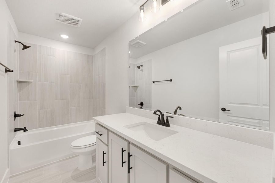 Bathroom with white quartz vanity, tub-shower combo with tile surround, and black hardware accents