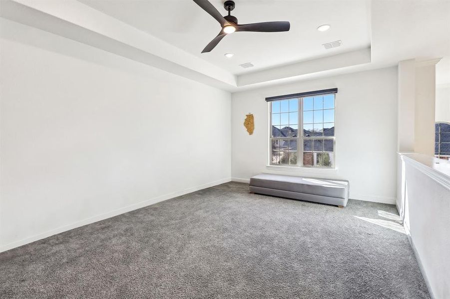 Carpeted empty room with baseboards, visible vents, ceiling fan, and a tray ceiling Carpeted empty room with baseboards, visible vents, ceiling fan, and a tray ceiling